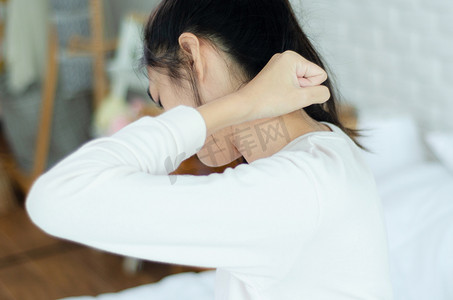 睡衣实体店摄影照片_亚洲女人在卧室里穿着白色睡衣。2.她的脖子有点痛.