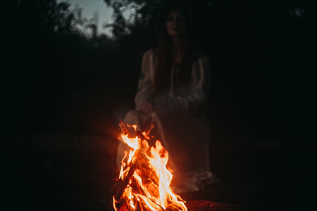 身穿民族服装、头上有小链的女子坐在篝火旁。异教徒假期的概念.