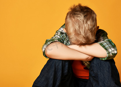 boy摄影照片_Blond boy child in checkered shirt sitting and covering face eyes with hands looking down