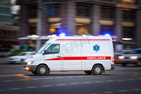 焦点摄影照片_救护车在一个宽阔的城市街道上。白色的紧急车辆，装有警示灯和警笛，快速驶过一条大道。大都市救援服务运输。运动模糊和选定的焦点