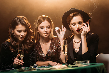 有吸引力的女孩与香槟, 香烟和扑克筹码一杯坐在桌子上, 看着赌场的扑克牌