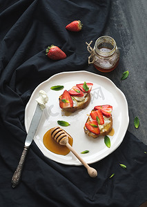 薄荷奶酪摄影照片_法国吐司与草莓、 奶油奶酪、 蜂蜜和薄荷光陶瓷板在黑色背景上