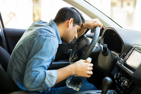 喝醉的人用手在车上睡觉。年轻醉酒司机与一瓶威士忌.