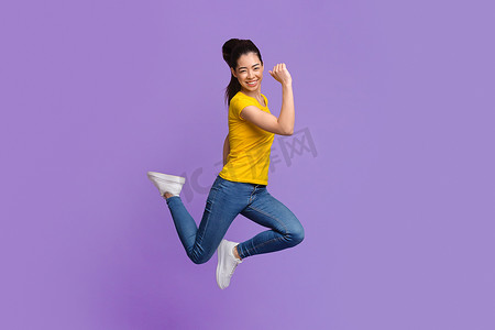 喜形于色的亚洲女孩在紫色工作室的背景上举起拳头跳了起来