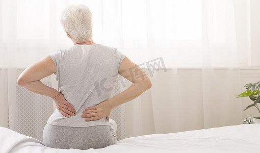 老年妇女抱着她痛苦的背部在床上