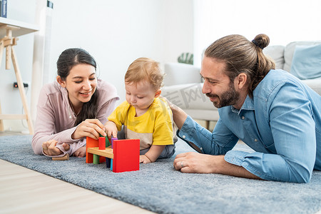 白人快乐可爱的父母在客厅里和蹒跚学步的小孩玩耍。迷人的夫妻父母期待着幼儿的发育。家庭内部的活动关系.