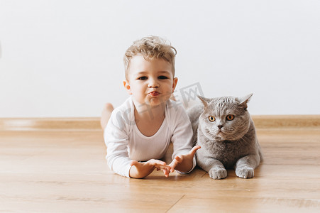 可爱的学步男孩和灰色英国短毛猫猫躺在地板上一起在家