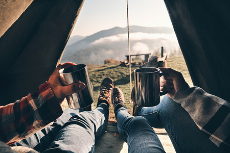 部分看法, 接近的夫妇欣赏山脉的看法, 而躺在帐篷与热饮料在杯子