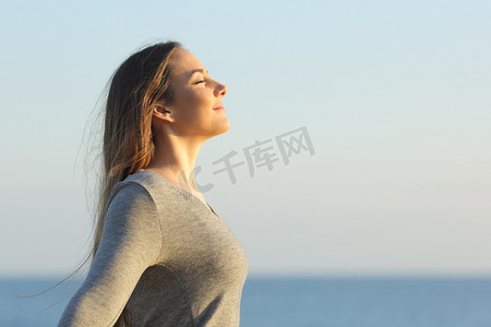 一位在海滩上呼吸新鲜空气的悠闲女子的侧景画像