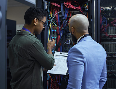 Explaining the ins and outs. two male IT support agents working together in a dark network server room