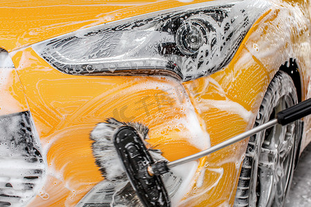 前前前前前前大灯和保险杠的黄色汽车被洗在自助洗车, 刷子离开笔触在洗发水和泡沫.