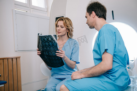 圆心放射线摄影照片_细心的放射技师看着坐在ct扫描仪床上的病人附近的X射线诊断