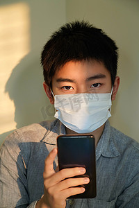 学生防疫摄影照片_戴口罩的男孩看手机
