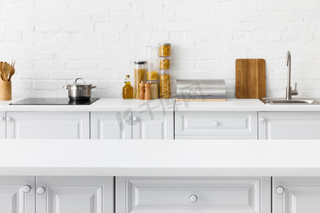 现代简约厨房摄影照片_选择重点的空桌和简约的现代白色厨房内部与厨房用具和食物靠近砖墙的背景