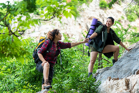 团体远足妇女帮助她的朋友爬上落山的最后一段。旅行团团队精神走在户外生活冒险和露营中.旅行概念.