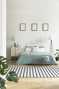 明亮的卧室内部的真实照片与三个简单的海报, 条纹地毯和粉彩绿床单在双人床上
