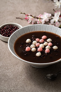 将红白相间的汤圆（汤圆，糯米团）与甜红豆汤一起放在灰色桌子上的碗里，准备过冬.
