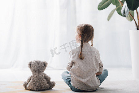 小孩子坐在地板上与泰迪熊的后视镜, 并把目光移开