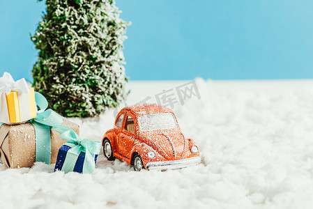 玩具车的特写镜头与礼物和圣诞树站立在由棉花制成的雪在蓝色背景
