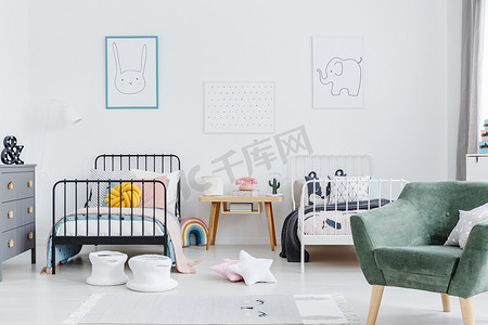 明亮斯堪的纳维亚风格的卧室内部有两个金属框架儿童床, 一个白色, 一个黑色, 和绿色的扶手椅为看守。一只兔子和一只大象在白墙上的海报。真实照片