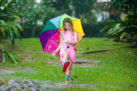 孩子在雨中玩耍。孩子们穿着雨伞和雨靴在外面大雨倾盆地玩耍.小女孩在泥泞的水坑里跳跃.孩子们被秋天的雨天逗乐了.在热带风暴中奔跑的儿童.