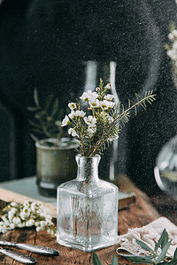 春天的花朵和绿色的装饰在桌子上, 在玻璃瓶里用水和水滴在玻璃上。温暖的伽玛和克制的成分, 小花和草, 在一个黑暗的木质背景