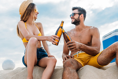 美丽的年轻夫妇无比与瓶啤酒, 而坐在沙滩上