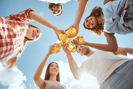 享受夏天的快乐时光。快乐的年轻人在啤酒的叮当声中，在蓝天的映衬下微笑着。烧烤的概念.