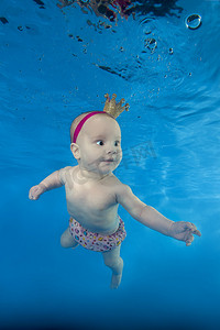一个戴皇冠的小女孩在水池水下游泳
