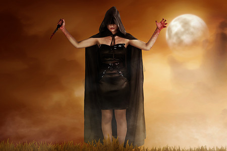 年轻的巫婆妇女在黑帽状斗篷持有血淋淋的刀与戏剧性场面背景