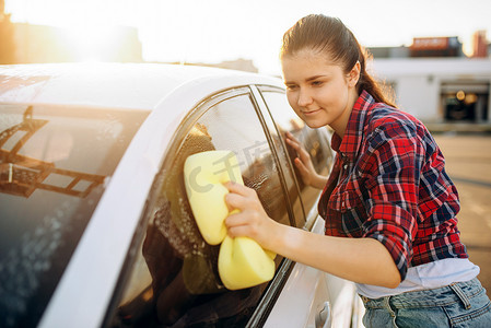 年轻女子用海绵擦洗车玻璃用泡沫, 洗车。女士在自助洗车。户外洗车