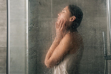 沮丧的女人摄影照片_悲伤的沮丧的女人在淋浴通过玻璃与水滴
