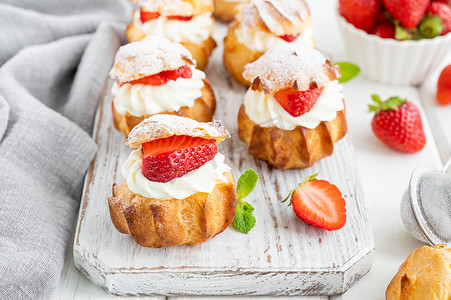 奶油风吊灯摄影照片_美味的自制小蛋糕，用奶油、草莓和糖粉装饰在白色的木制背景上。复制空间