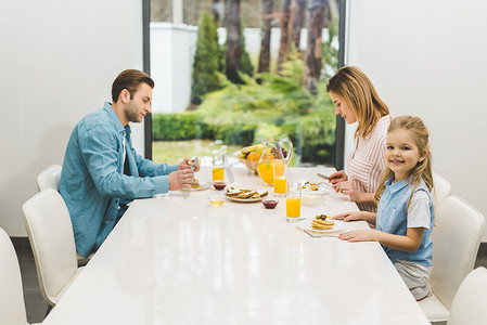 父母和小女儿在家里一起吃早饭的侧面视图