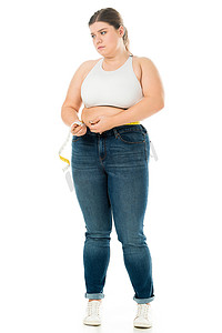 不满意超重妇女在牛仔裤测量腰部用测量带查出在白色, 减肥概念