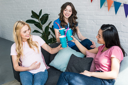 多文化的朋友和怀孕的妇女在婴儿聚会上用纸杯喝杯酒无比。