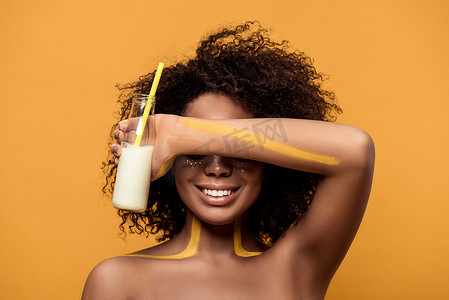 年轻微笑的非洲裔美国妇女与艺术性的化妆藏品瓶与牛奶隔绝在橙色背景