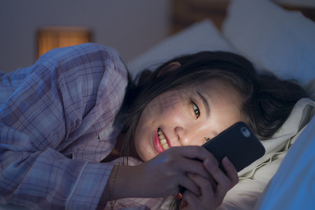 pajamas摄影照片_young beautiful and happy sweet Asian Korean woman with in pajamas enjoying with mobile phone app in bed at night in internet social media addiction concept