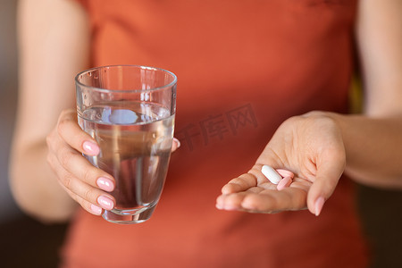 一堆药丸摄影照片_无法辨认的女人手里拿着一杯水和一堆堆药丸，被女人用维生素补充剂擦伤美体和免疫力，或接受治疗，被剪裁的形象