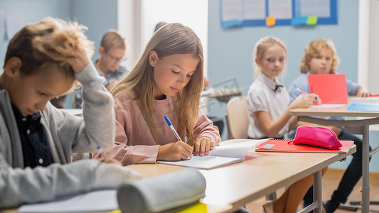 孩子们摄影照片_不同儿童的小学课堂认真听老师讲课。在学校里聪明的孩子们在练习本上写作，参加考试和考试。儿童学习