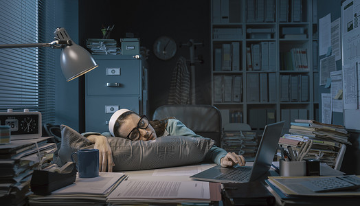 Exhausted young office worker sleeping at her desk, job burnout and overtime work concept
