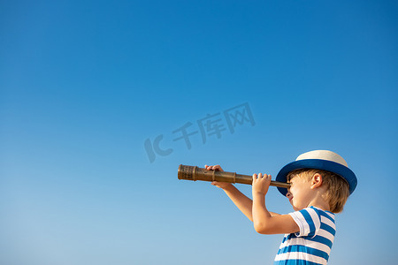 小孩透过望远镜望着蓝天.孩子夏天在户外玩得很开心.冒险和旅行概念