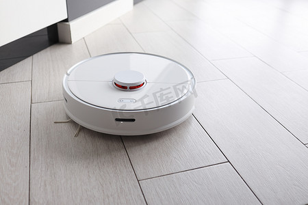 modern摄影照片_Robot vacuum cleaner removes dust in room on floor. Vacuum cleaner in ordinary apartment. modern household wireless device for cleaning house. smart home concept.