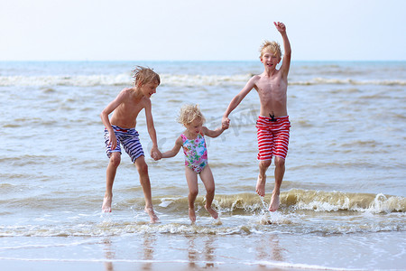 小孩跳摄影照片_Kids having fun on the beach jumping over the waves