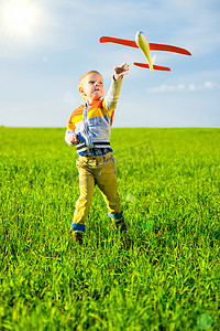 banner图绿色摄影照片_快乐的男孩玩玩具飞机攻击蓝色夏天天空和绿色领域背景.