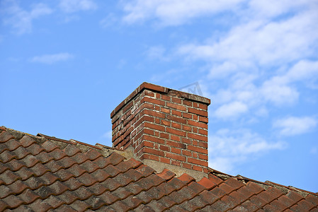 Red brick chimney designed on slate roof of a house building outside with blue sky background and copyspace. Exterior construction architecture of escape chute on rooftop for fireplace smoke and heat.