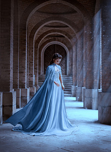 悲伤的雪女王走在古老的城堡里。 蓝色丝绸长雨衣列车飞行运动。 精灵的发型可爱的脸。 复古奇幻艺术复古风格。 《冰雪奇缘》女性摄影。 太阳魔法光芒
