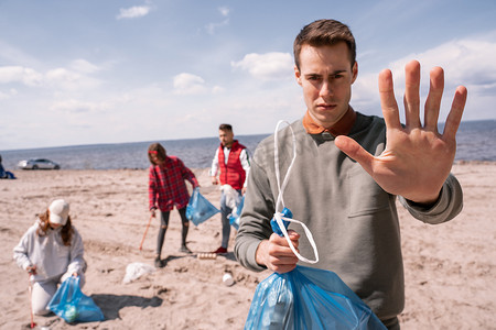年轻男子在接近一群捡垃圾、生态概念的志愿者时表现出停下来的姿态 