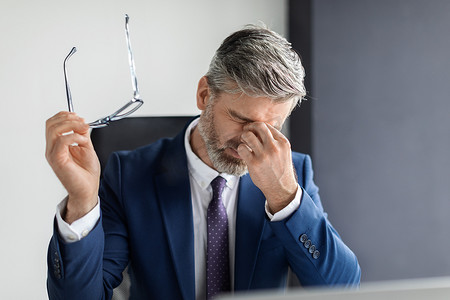 Portrait Of Tired Middle Aged Businessman Suffering Eye Strain At Workplace, Stressed Mature Male Entrepreneur Man Sitting At Desk, Taking Off Glasses And Massaging Nosebridge, Free Space