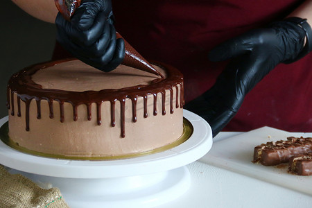 液体巧克力摄影照片_糖果店加工桌上的巧克力蛋糕。用液体巧克力装饰蛋糕的过程.在深色背景下制作巧克力蛋糕的过程